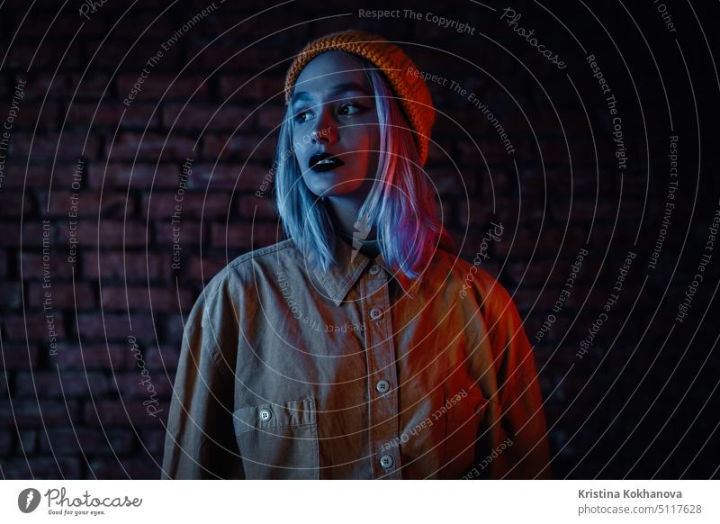 Young woman in pink and blue neon light. Portrait of unusual beautiful punk girl with colorful hairstyle on bricks wall studio background teen emotions