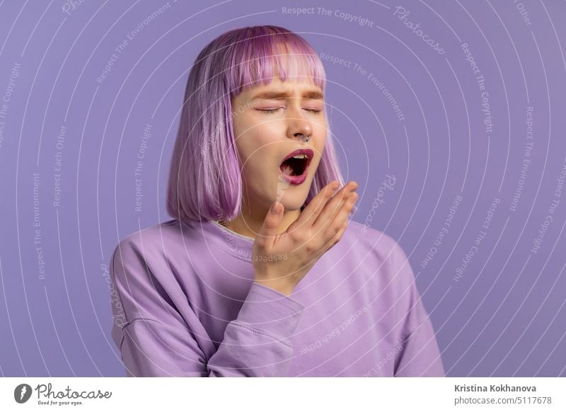 Tired sleepy woman yawns, covers her mouth with hand. Very boring, uninteresting. Violet studio background. person face young tired guy indoor adult yawning