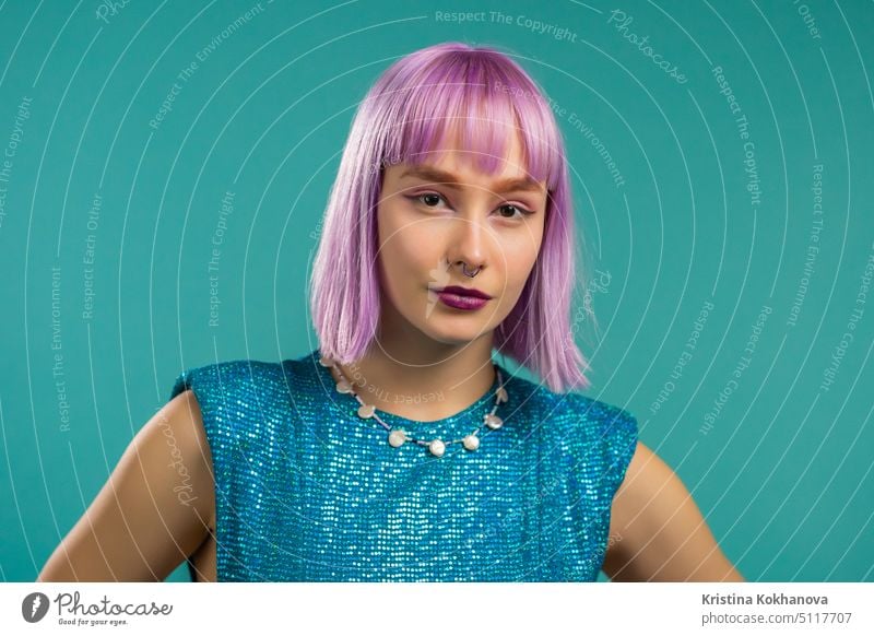 Portrait of hipster woman with dyed violet hair over turquoise studio background. Positive young party girl looking to camera. Amazing sparkling outfit person