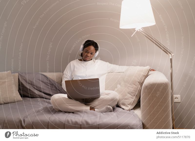 Black woman using laptop on sofa living room movie evening pajama addict rest female black african american ethnic young online home browsing couch cozy