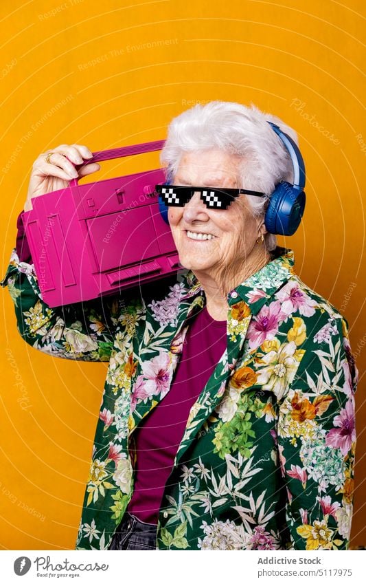 Optimistic aged meloman with boombox woman smile listen music style carry happy colorful bright female elderly senior pensioner retire headphones wireless