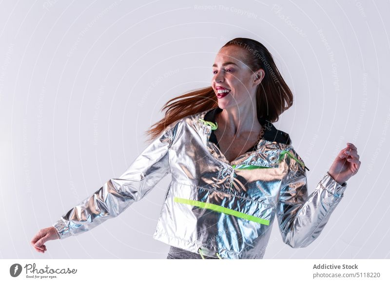 Cheerful woman in foil jacket dancing in studio smile model long hair dance futuristic style makeup fashion trendy appearance happy cheerful young female