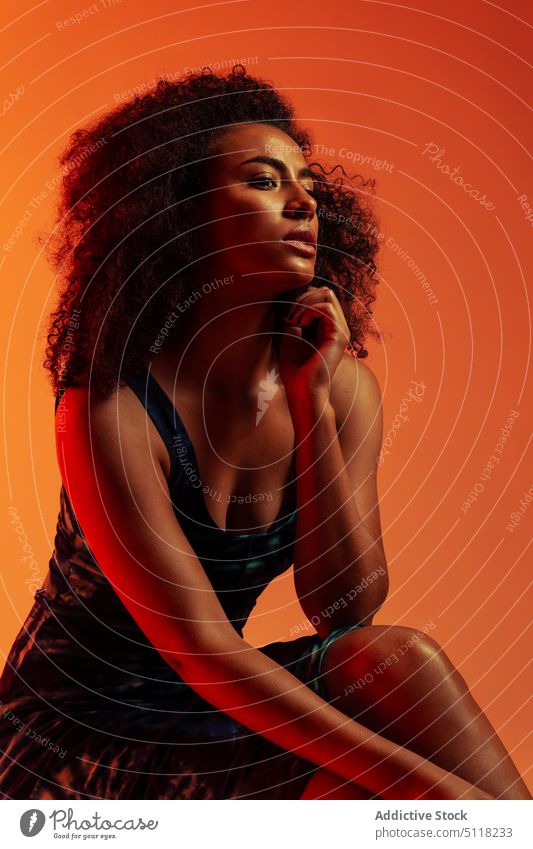 Alluring ethnic female in dress woman sensual allure model touch chin legs crossed fashion afro studio shot style feminine appearance elegant african american