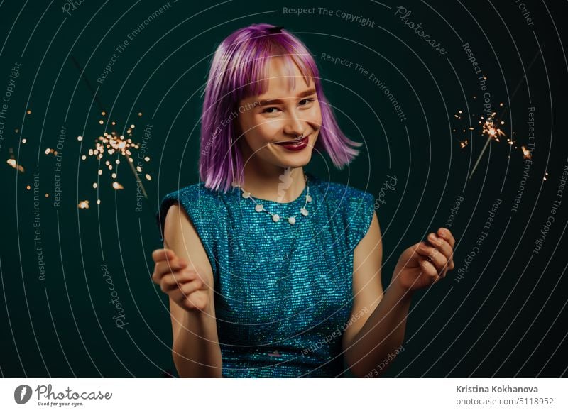 Hipster woman with sparkling bengal fire on green background. Christmas holiday concept. Young dyed violet haired girl with sparkler celebrating, smiling, enjoying time.