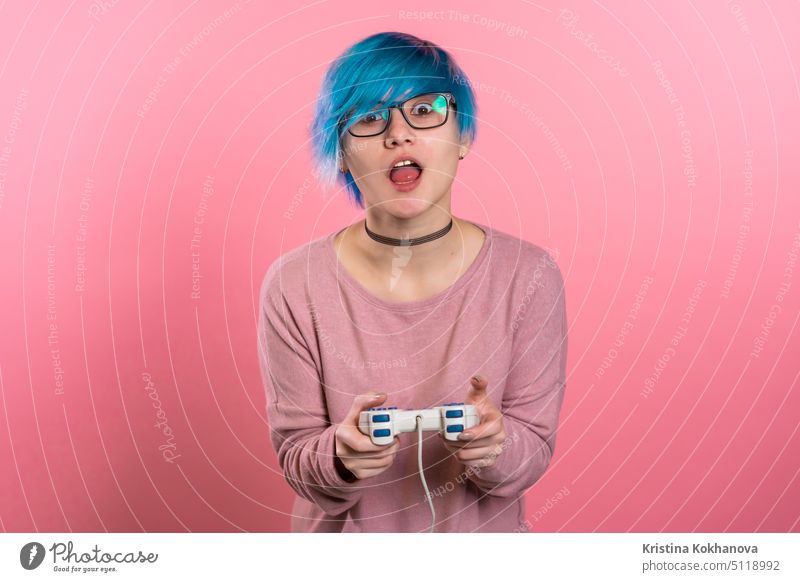 Pretty young girl with blue hairstyle playing video exciting game on Tv with joystick on pink studio wall. Using modern technology. fun indoor console man