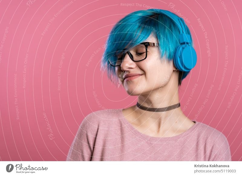 Pretty young girl with turquoise hair having fun, smiling, dancing with blue headphones in studio on colorful background. Music, dance, radio concept. woman