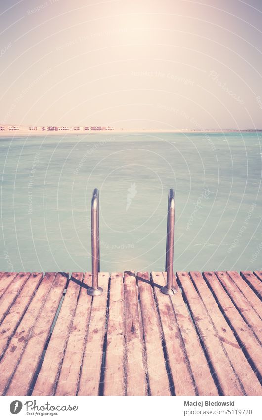 Retro color toned picture of a wooden pier with swim ladder. retro water vacation sky nature sea summer resort board travel horizon empty ocean sunny tranquil