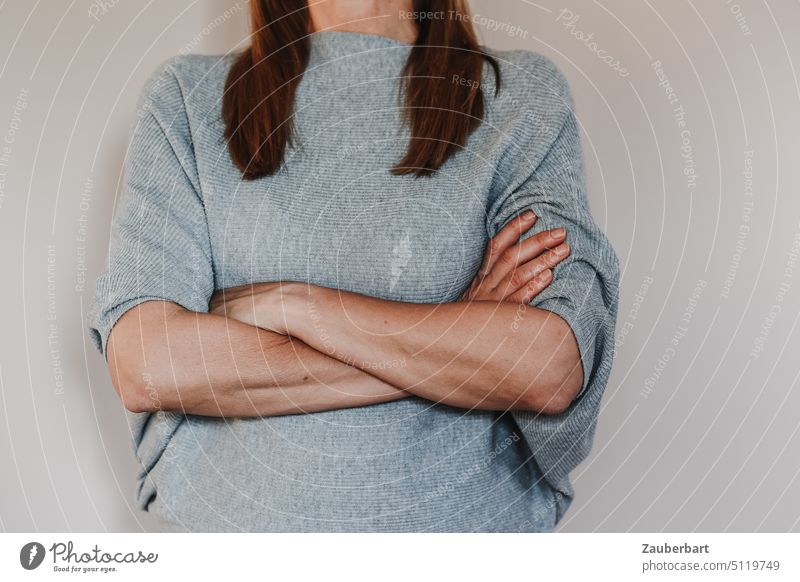 Woman with folded arms, light blue sweater, in front of neutral background Arm Interlocked no defense determined Upper body arms folded Self-confident Strong