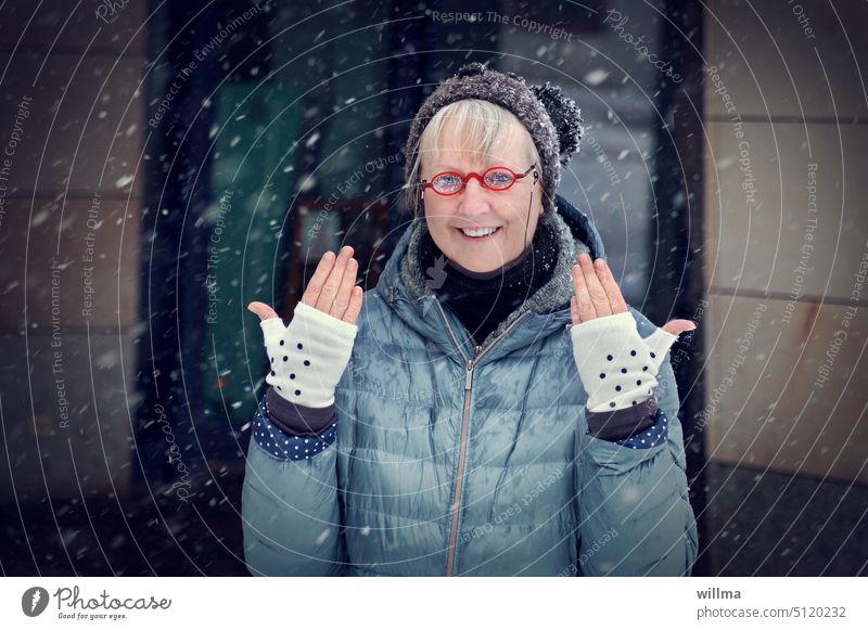 Older woman with red glasses and bobble hat laughs and shows her gloves with dots Woman Winter Gloves cheerful Eyeglasses fingerless gloves hands Joy Cap