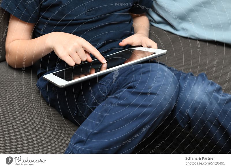 Child sitting on couch with tablet on lap and tapping screen with one finger New Media Ipad media consumption Sit Cozy School free time family life Infancy