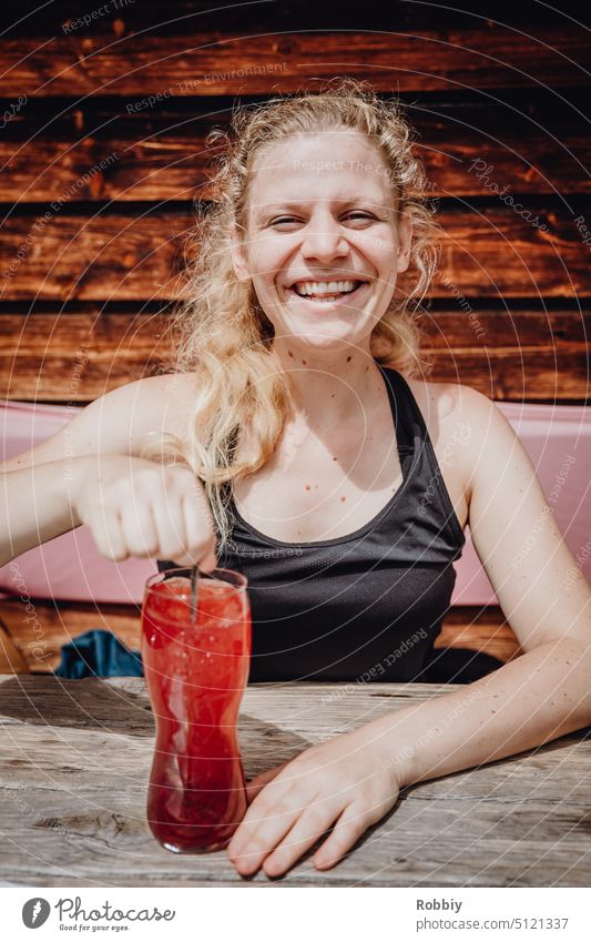 A young blonde woman with a drink at a wooden table Young woman Blonde smilingly smiling woman Laughter kind Looking into the camera Alpine hut Hut Break rest