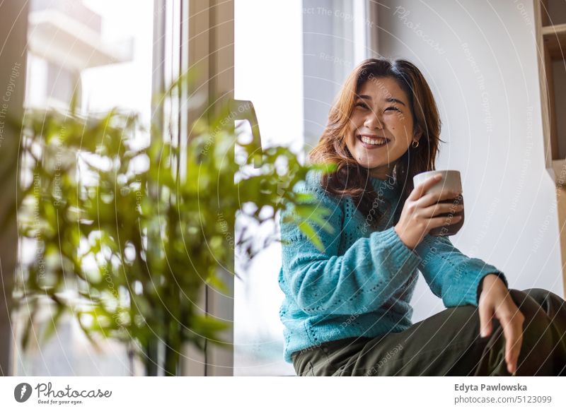 Young woman drinking a cup of coffee in her apartment real people candid girl young adult fun millennials Millennial Generation asian Japanese happy smiling