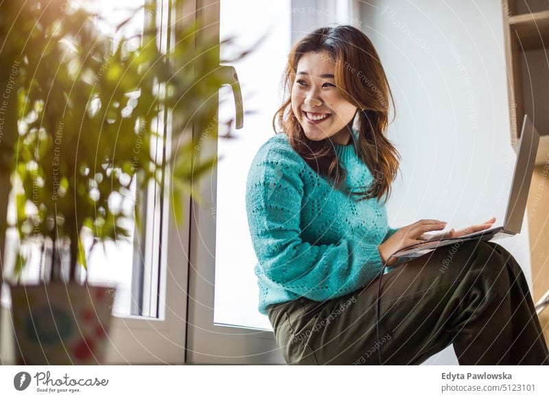 Young woman using laptop in her studio apartment real people candid girl young adult fun millennials Millennial Generation asian Japanese happy smiling