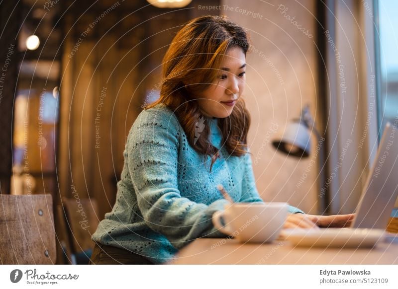 Young woman working on laptop in coffee shop real people candid girl young adult fun millennials Millennial Generation asian Japanese happy smiling happiness