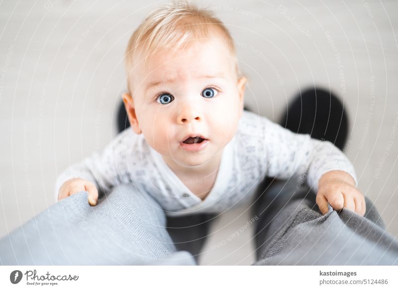 Top down view of cheerful baby boy infant taking first steps holding to father's sweatpants at home. Cute baby boy learning to walk little child happy dad small
