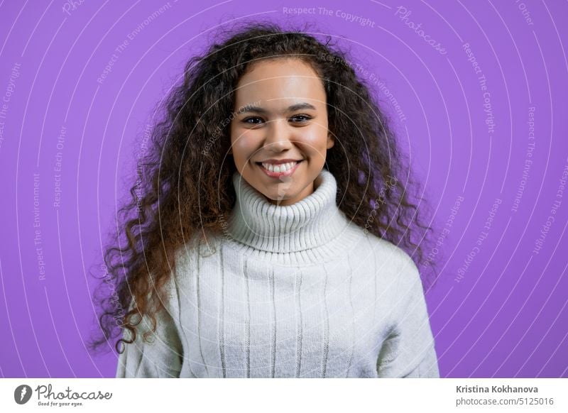 Portrait of pretty woman on violet studio background. Positive young girl with natural curly hair, she in white sweater smiles to camera. person success