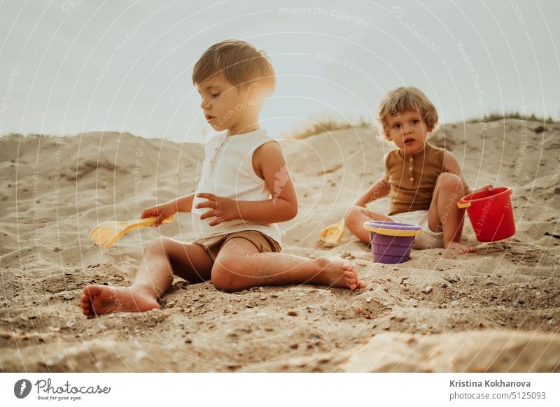 Twin brothers play on beach in sand with their plastic toys. Summer sunny day. Cute friends, children, family concept. fun summer person vacation sea joy kid