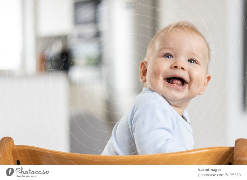 Happy infant sitting in traditional scandinavian designer wooden high chair and laughing out loud in modern bright home. Cute baby smile. child happy cute kid
