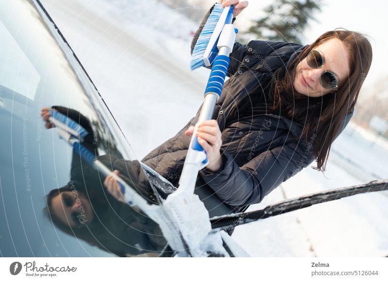 Woman cleans car with a brush from snow after a blizzard cleaning cold female glass hand holding person removal safety seasonal snowfall snowstorm blue tool
