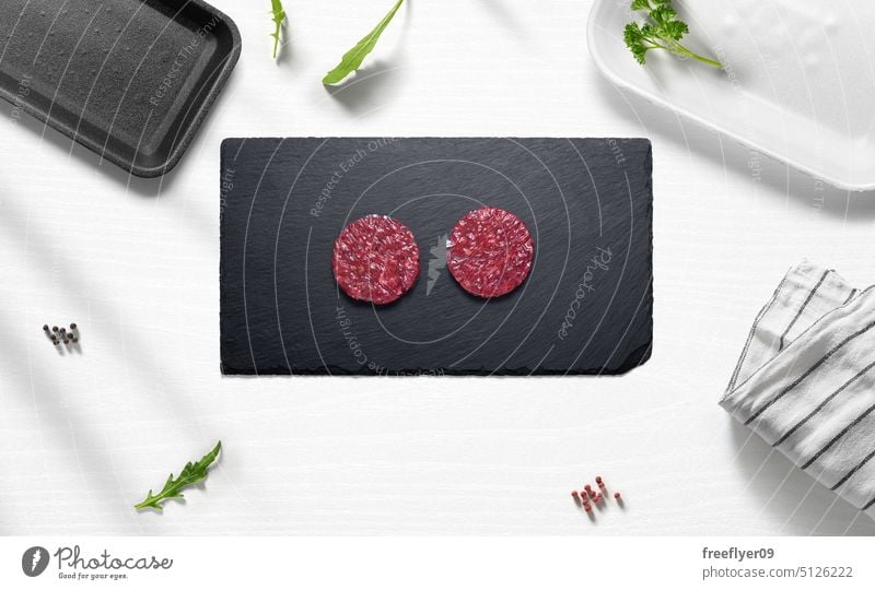 Beef mini hamburgers on a flat lay of a kitchen with various items hamburguer beef meat piece raw butcher shop copy space pepper parsley arugula cutting board