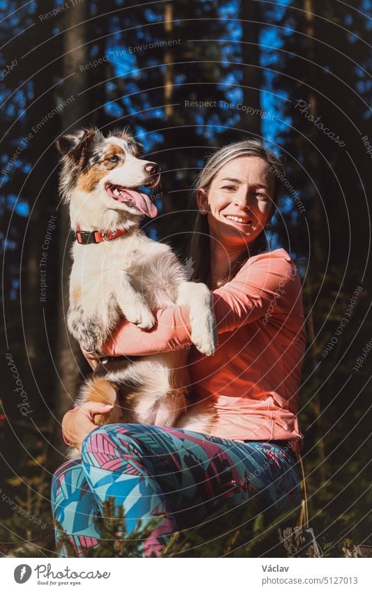 Candid portrait of a young female athlete with her running and hiking partner, an Australian Shepherd dog. Realistic smile of woman and dog. Happy couple. Blue merle and hiker