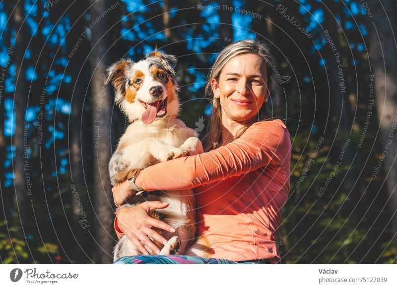 Candid portrait of a young female athlete with her running and hiking partner, an Australian Shepherd dog. Realistic smile of woman and dog. Happy couple. Blue merle and hiker