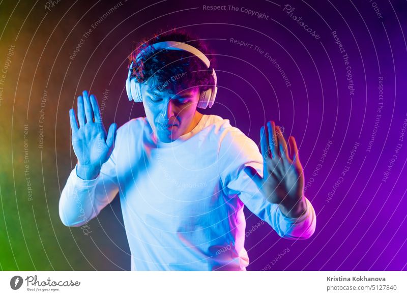 Positive man listening music with headphones, dancing on dark neon background. Stylish student guy enjoying life, active energy, inspired dance concept action