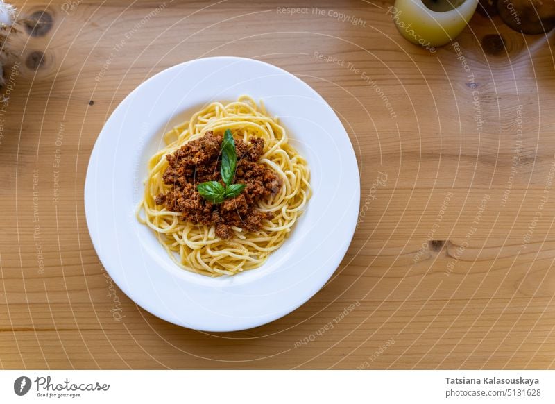 Spaghetti bolognese in white plate, decorated with basil leaf on wooden table, View from above. Classic dish of Italian cuisine. Pasta Bolognese Sauce