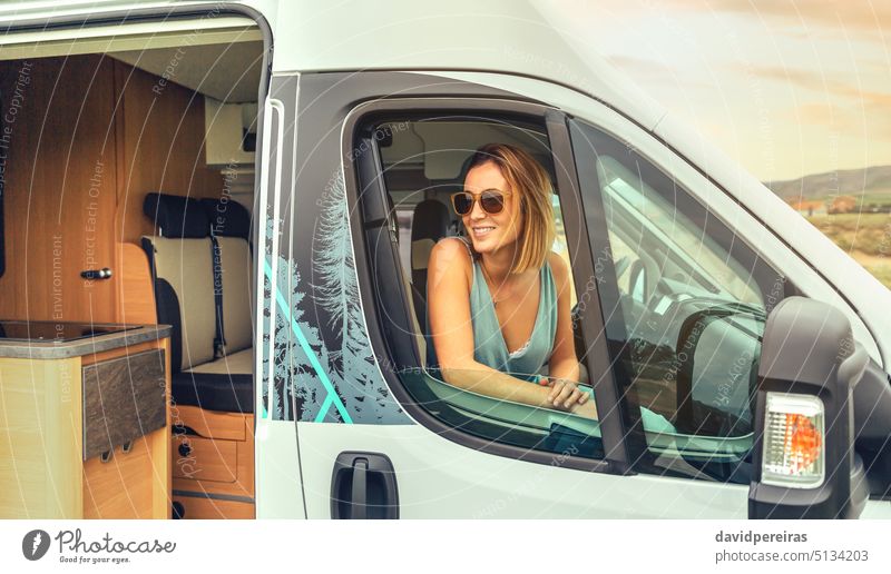 Young woman in sunglasses sitting in camper van smiling young summer trip travel journey vehicle freedom 20s person female tourist car happy cheerful carefree