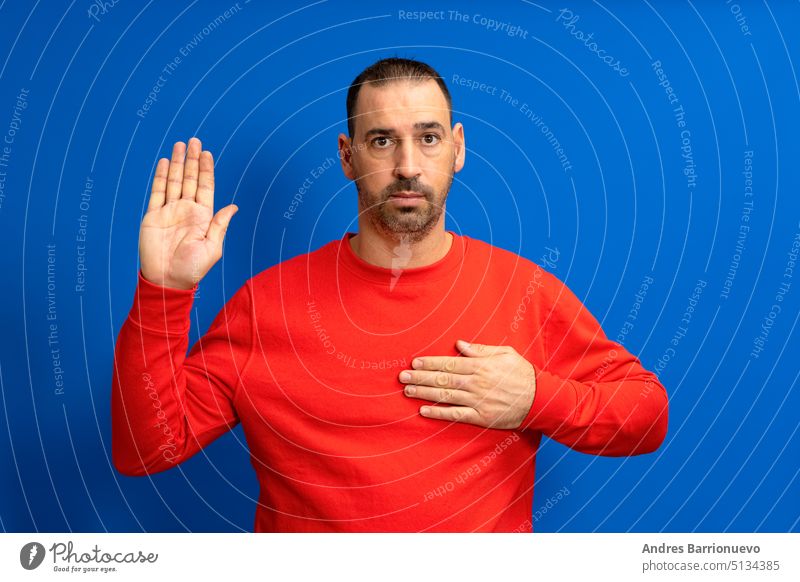 Photo of serious and confident bearded hispanic man with hand on chest promising oath isolated over blue colored background. handsome gesture pride justice