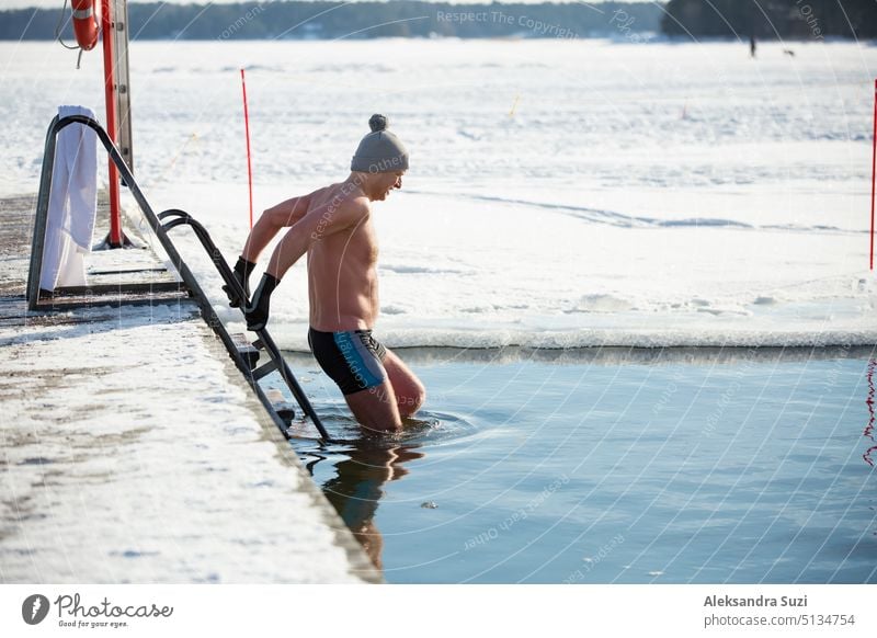 A man in warm hat and gloves swimming in an ice hole, walking along the pier. Winter activities in Finland. Healthy lifestyle active activity adult alternative