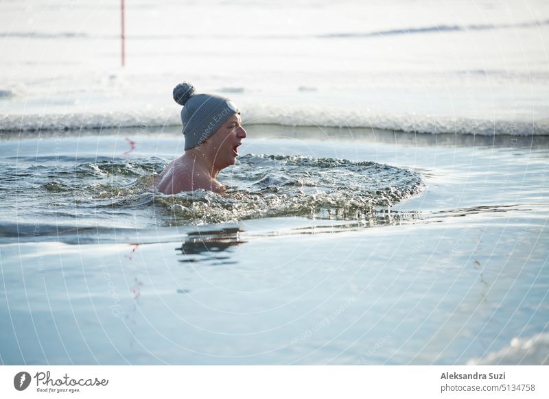 A man in warm hat swimming in an ice hole. Winter activity in Finland. Healthy lifestyle active adult alternative bathing body care cold dive enjoyment exercise
