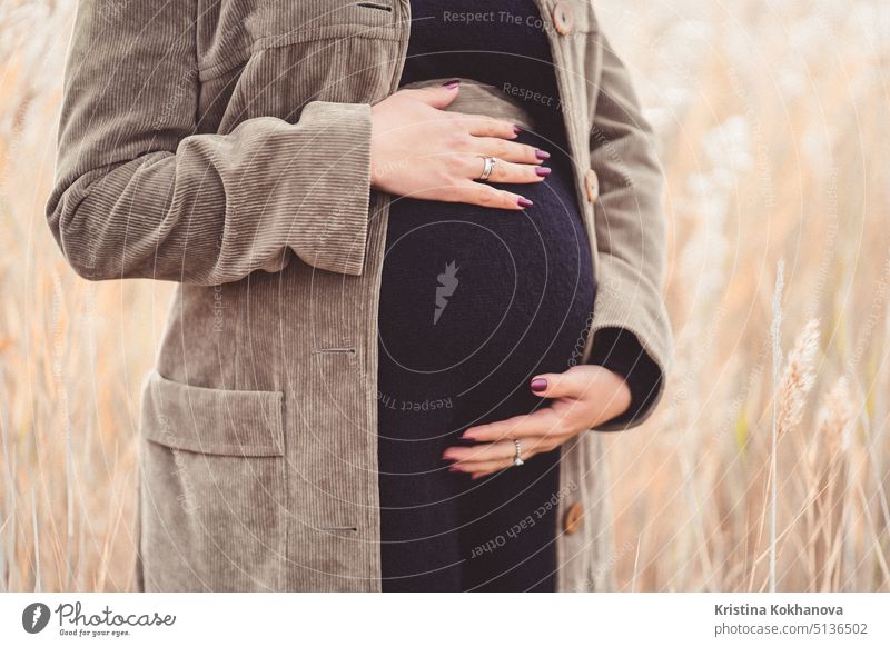 Pregnant unrecognizable woman in black dress standing in reeds and holding her belly. pregnant mother maternity pregnancy tummy abdomen baby beautiful female