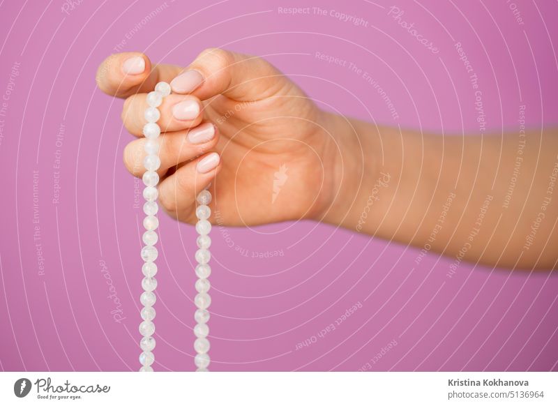 Woman, lit hand close up, counts Malas, strands of gemstones beads used for keeping count during mantra meditations on pink background mala rosary prayer