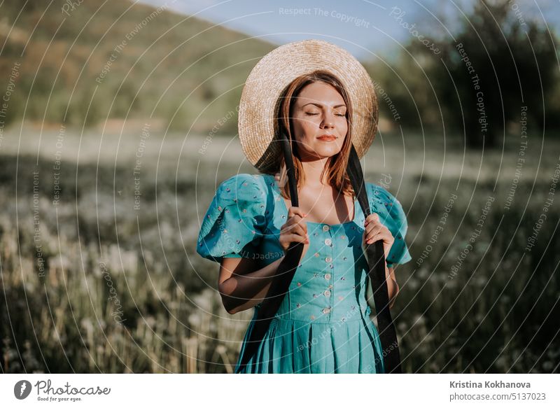Young stylish woman in vintage dress and straw hat alone on nature in countryside. Carefree lifestyle, romantic girl. Retro fashionista like from novel elegant
