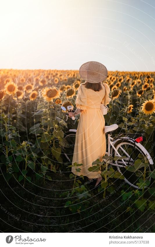 Attractive woman in timeless dress with retro styled bicycle in sunflowers field. Vintage fashion, amazing adventure, countryside activity, healthy lifestyle.