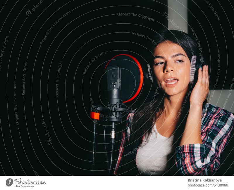 Young beautiful brunette woman recording voice, song or album in professional studio. Girl sings near microphone in recording room under natural light. artist