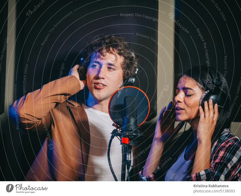 Two young singers performing their song in record studio. Professional musician duet recording new album CD. Beautiful couple working together. artist audio
