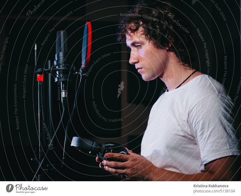 Young handsome singer man puts on headphones in the studio. Recording new melody or album. Male vocal artist with curly hair preparing for working audio