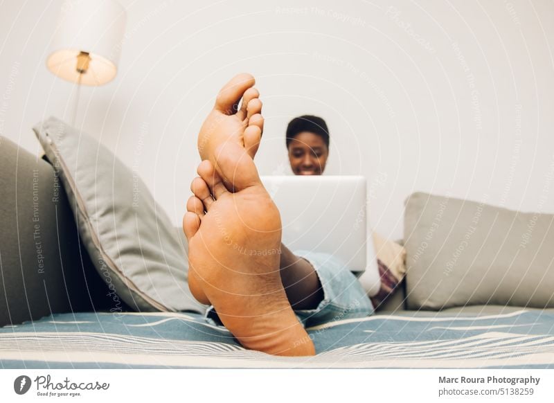 close up feet  of black woman using his laptop on a couch 20s adult barefoot beautiful bed bedroom candid portrait care casual cheerful closeup comfort computer