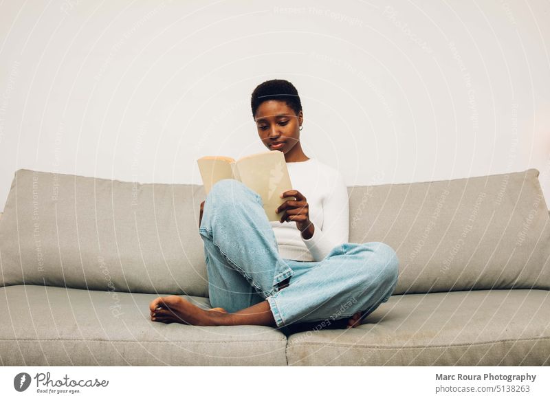 black woman reading on a sofa adult background beautiful book caucasian coffee comfortable couch drink education female girl happy hobby holding home indoors