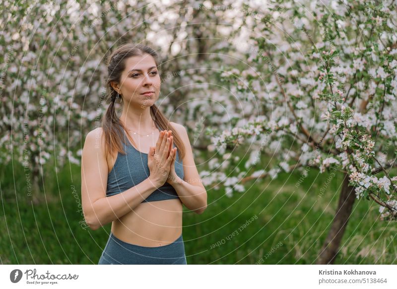 Woman with namaste yoga mudra hands on spring blossom garden natural background. Healthy girl training at outdoors. Gratitude, unity with nature, peace and love concept.