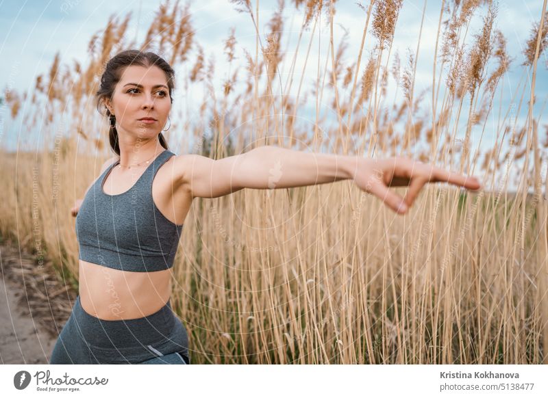 European woman doing yoga exercise on reed natural background. Concentrated girl training at summer outdoors. Pastel colors, unity with nature, balance, lifestyle concept.