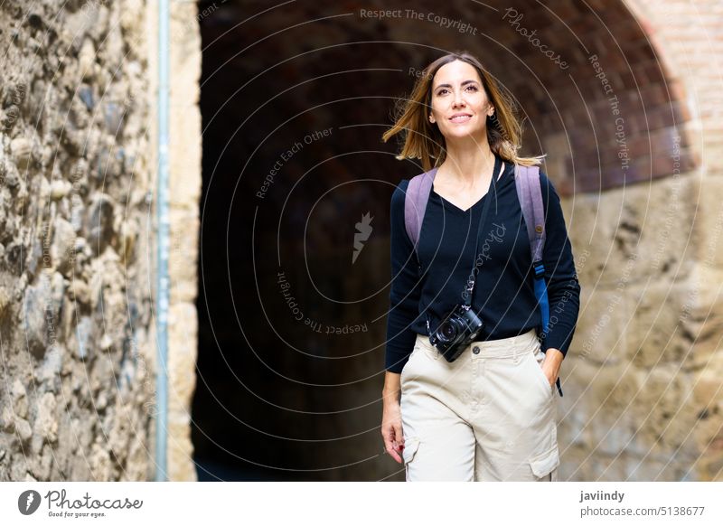 Positive woman smiling while sightseeing old city during holiday tourist smile walk archway happy vacation admire trip traveler female young casual photo camera