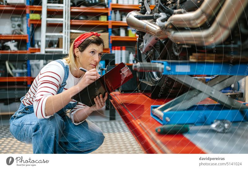 Mechanic reviewing damages in motorbike on workshop mechanic woman female checking inspection breakdown motorcycle platform garage factory insurance problem