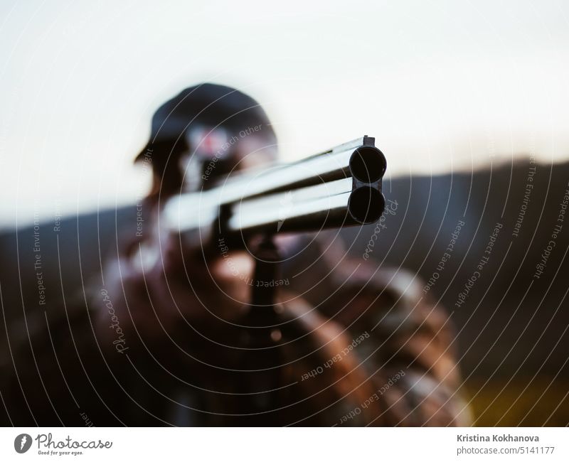 Close up of double barrel hunting gun. Hunter man wearing warm coat targets the enemy on the battlefield with rifle. Unrecognizable man hunts in the woods. Focus on barrel
