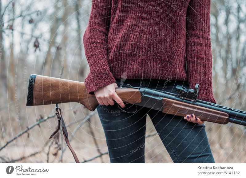 Hunter woman in burgundy warm clothes with gun. Girl hunting in the forest holding her rifle close up. activity adult aim aiming aristocracy autumn background