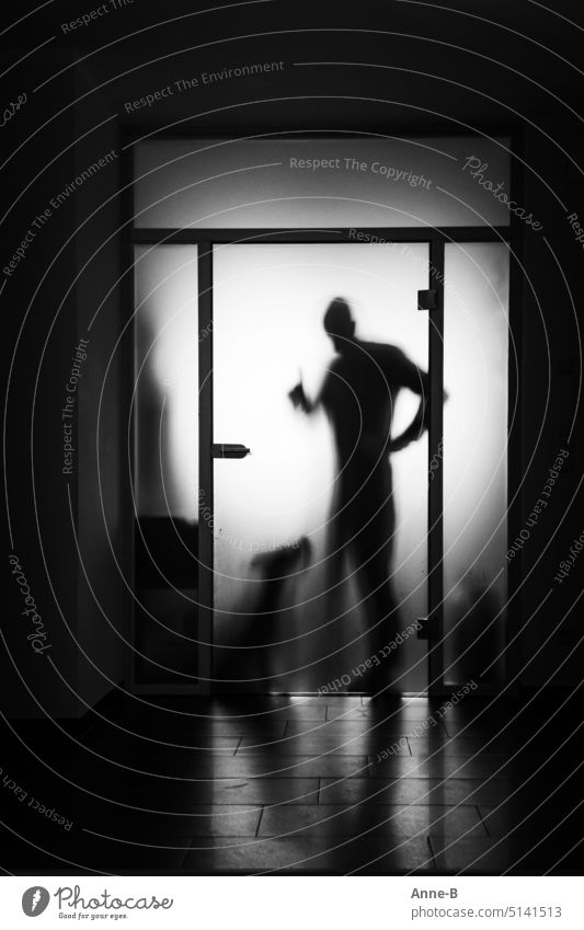 a man ( maybe a dog trainer ) asks a dog with raised index finger for attention behind the frosted glass pane of a door. dog training upbringing reprimand Dog