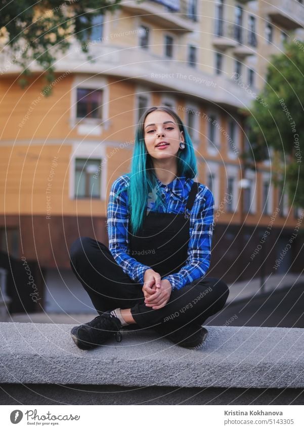 Hipster girl with blue dyed hair. Woman with piercing in nose, ears tunnels and unusual hairstyle having fun, posing in European city. Carefree concept.