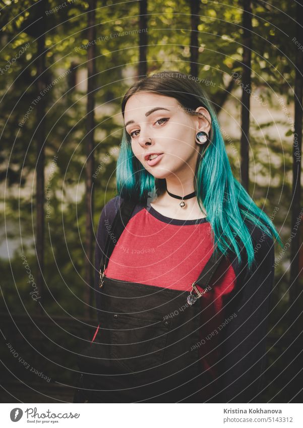 Street punk or hipster girl enjoying empty old European street. Portrait of teen girl with blue dyed hair,piercing in nose,violet lenses and unusual hairstyle.